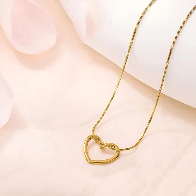 Gold heart pendant necklace resting on a soft pink and white background