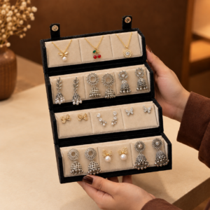 Person holding an open multi-tier black velvet jewelry box filled with necklaces and silver jhumka earrings.