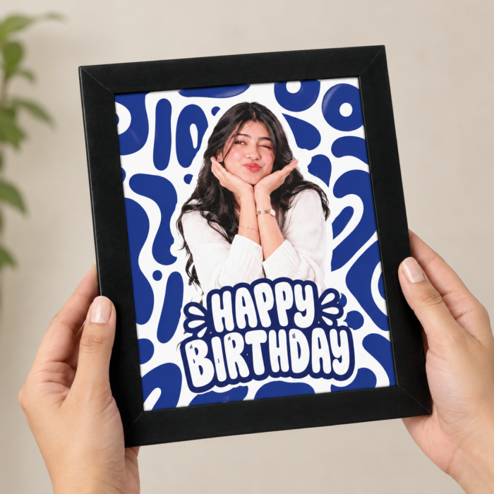 Hands holding a black framed custom photo print featuring a personalized photo, blue abstract backdrop, and Happy Birthday text.